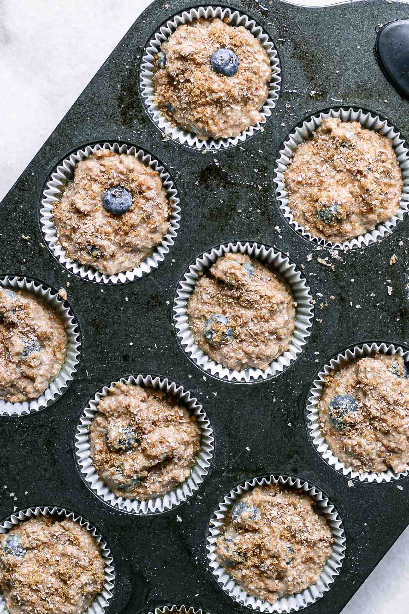 a muffin pan with uncooked blueberry bran muffin mix inside muffin liners before baking