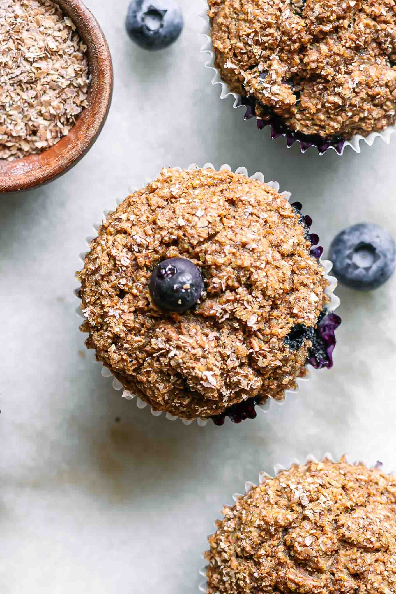 a close up photo of a plant-based blueberry bran muffins with fresh blueberries