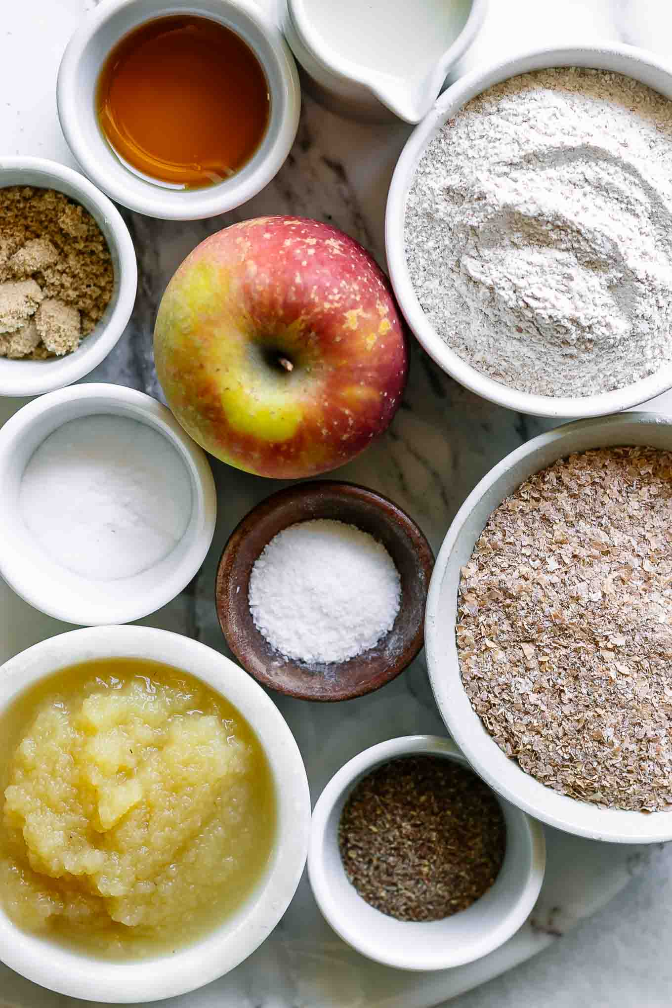bowls of wheat flour, wheat bran, apple sauce, apples, and other ingredients for apple bran muffins