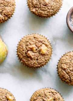 apple bran muffins on a table with a whole apple and bowl of wheat bran