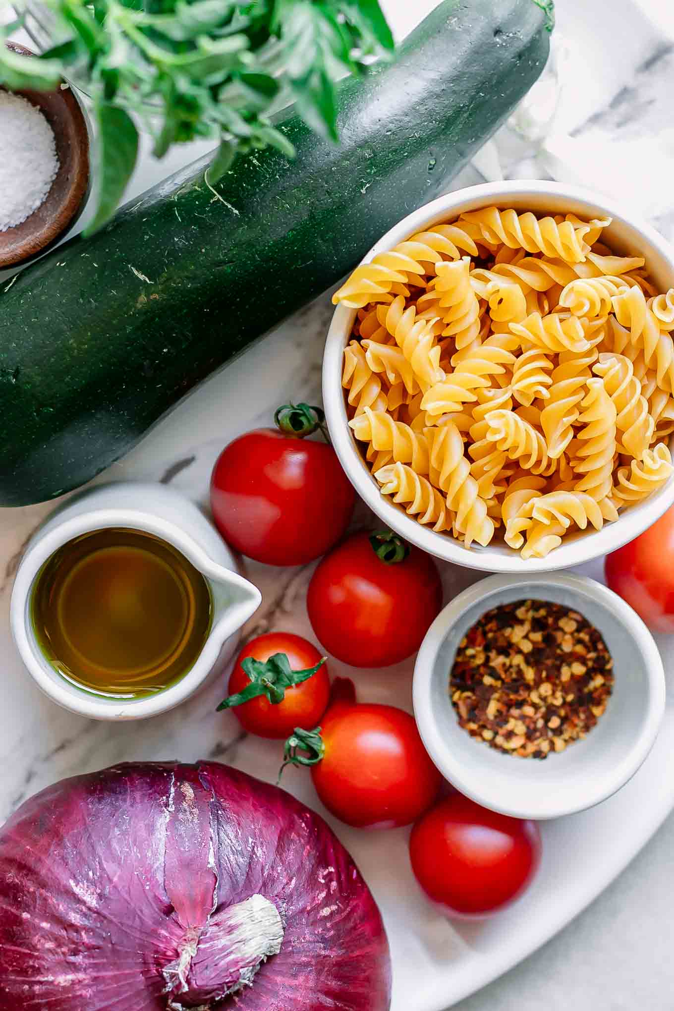 bowls of pasta, tomatoes, olive oil, and zucchini and basil on a white table for pasta