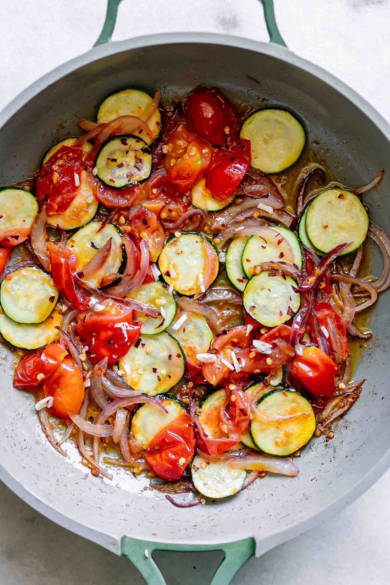a pan with zucchini, tomatoes, and red onion cooked in oil for pasta