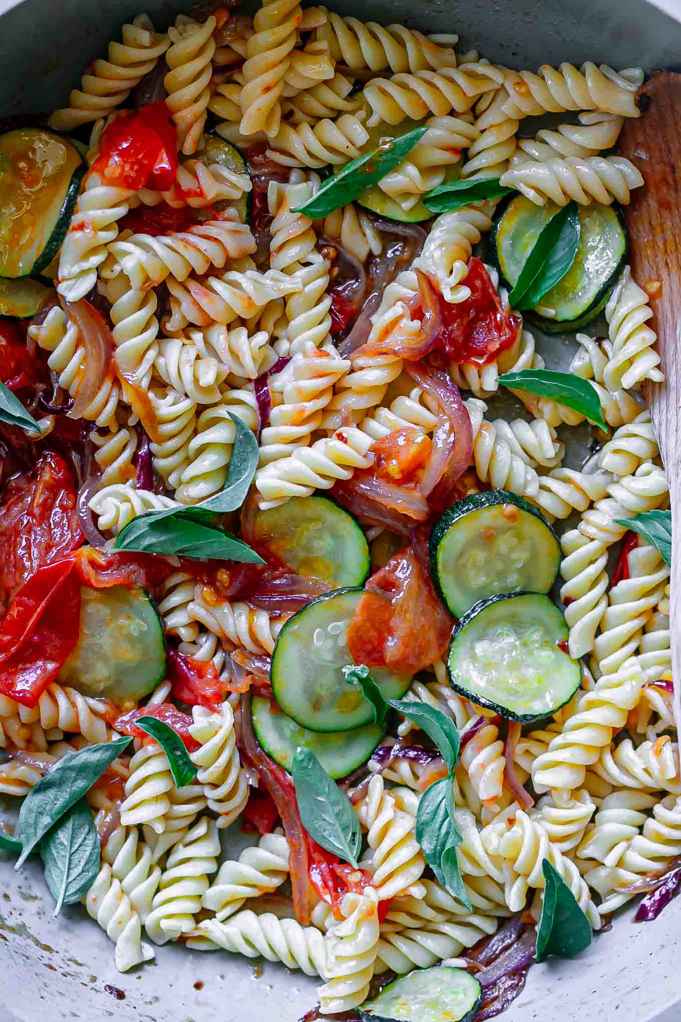 a close up photo of cooked pasta with zucchini, tomatoes, and fresh basil