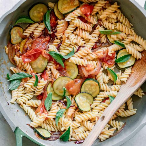 zucchini and tomato pasta with fresh basil in a pan with a spoon after cooking