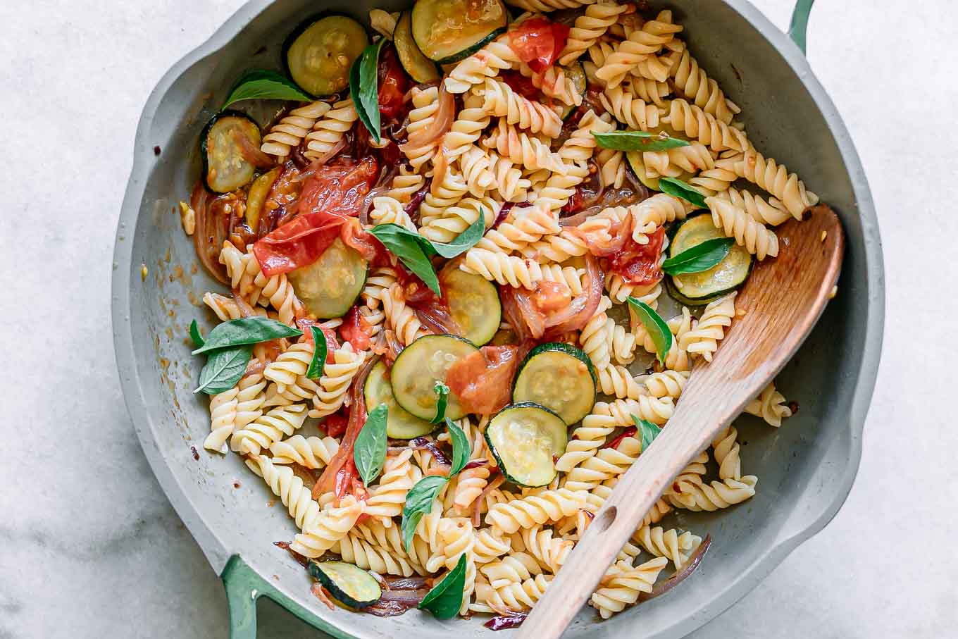 zucchini and tomato pasta with fresh basil in a pan with a spoon after cooking