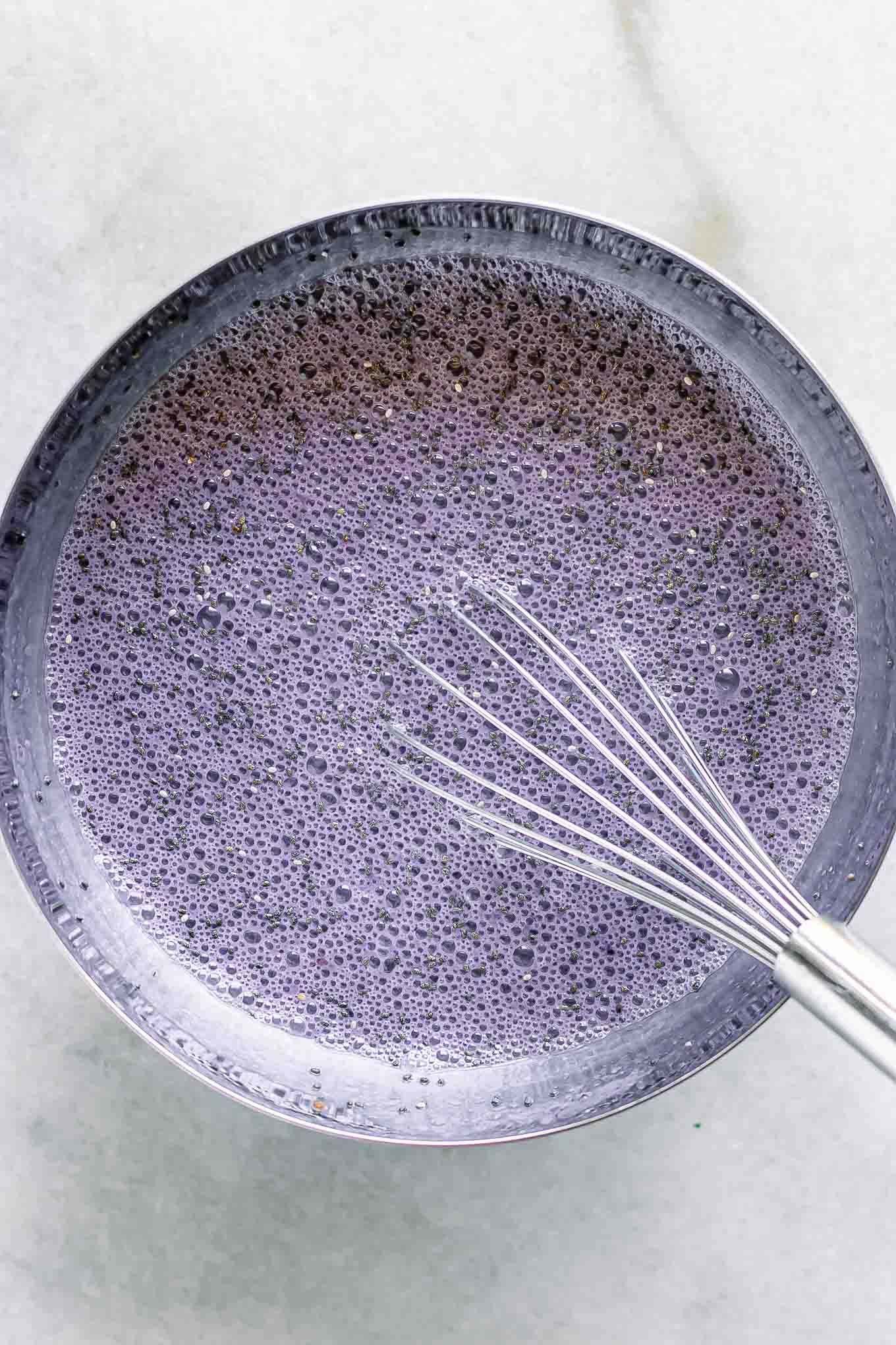 a bowl of blackberry chia seed pudding with a whisk on a white table