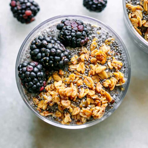 a close up photo of a glass of blackberry-flavored chia seed pudding with granola and fresh blackberries as garnish
