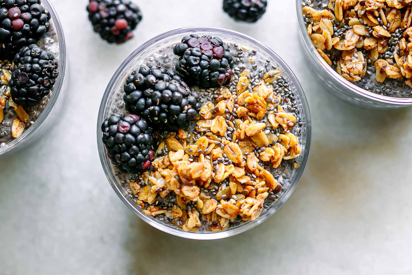 a close up photo of a glass of blackberry-flavored chia seed pudding with granola and fresh blackberries as garnish 