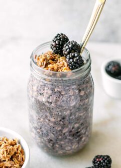 a mason jar with purple blackberry flavored overnight oats with a gold fork on a white table