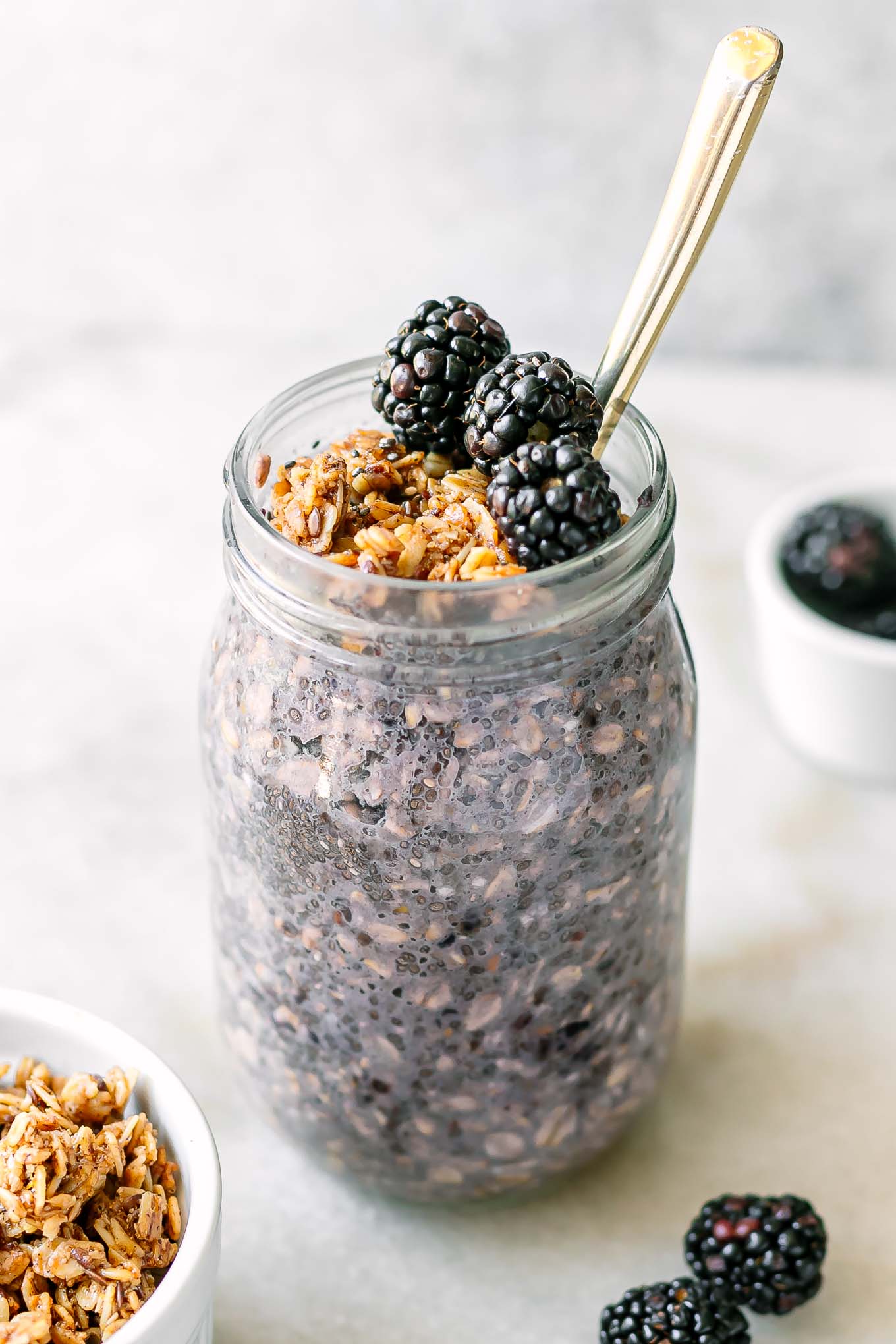 a mason jar with purple blackberry flavored overnight oats with a gold fork on a white table