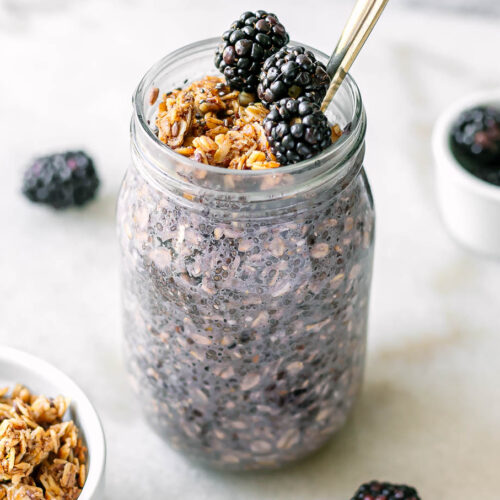a jar of blackberry chia seed pudding with granola and fresh blackberries on a white table