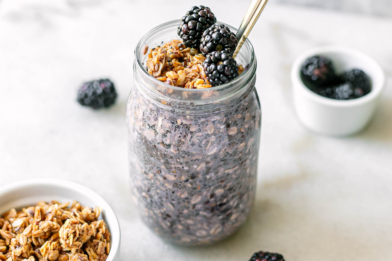 a jar of blackberry chia seed pudding with granola and fresh blackberries on a white table
