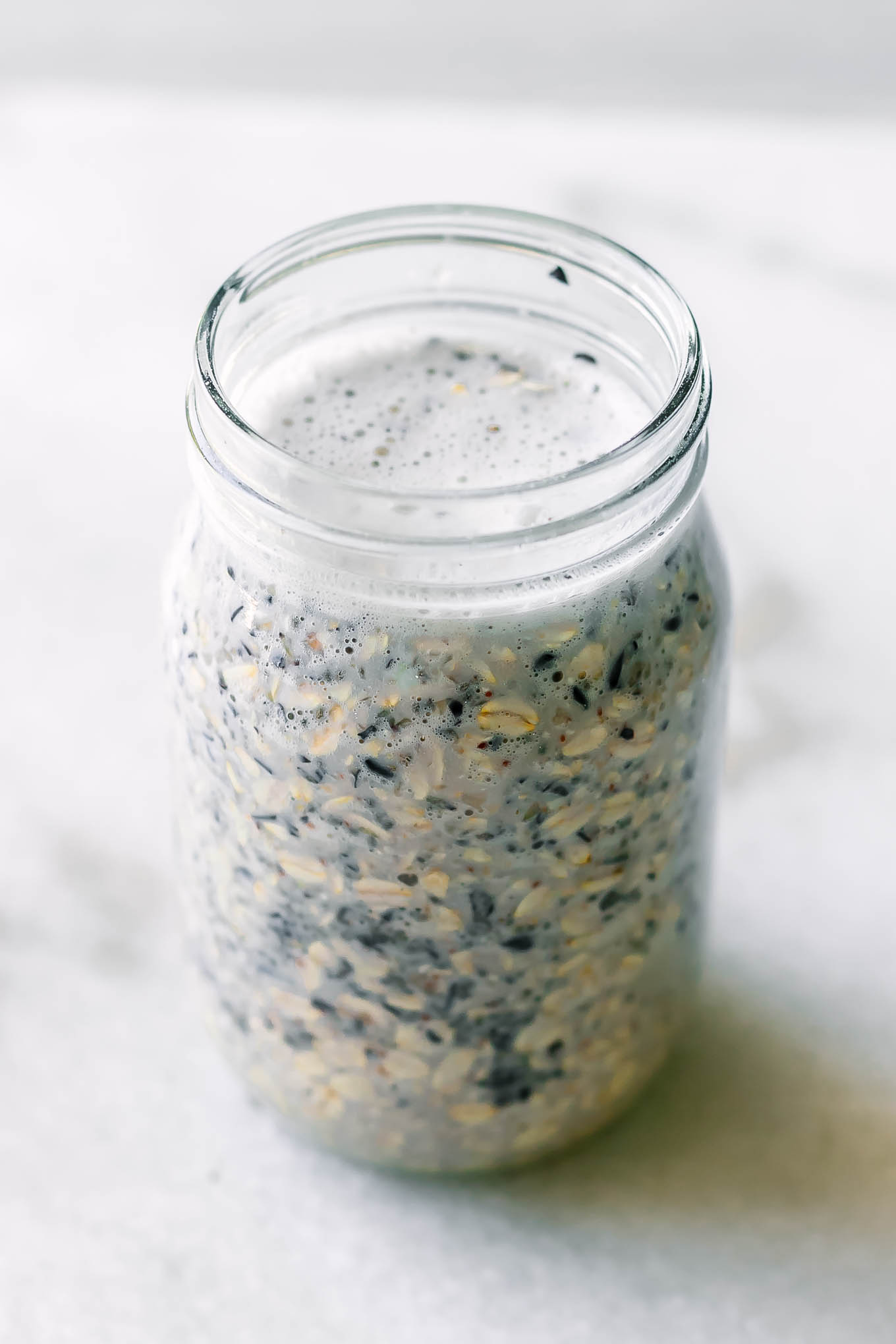 a mason jar with rolled oats, chia seeds, and blueberry milk for overnights oats on a white countertop