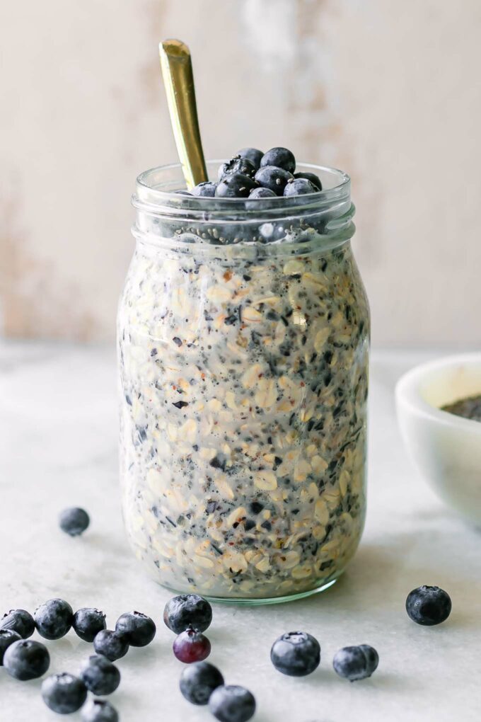 blueberry overnight oats in a mason jar on a white table with a gold spoon