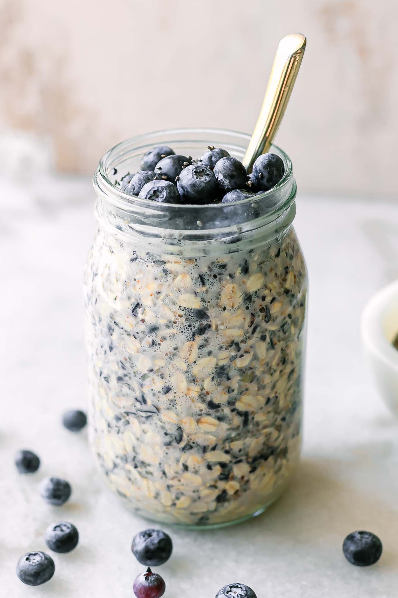 blueberry overnight oats in a mason jar on a white table with a gold spoon