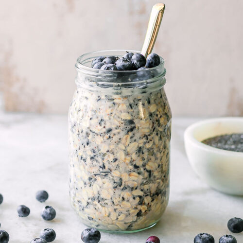 a jar of blueberry overnight oats with fresh blueberry garnish on a white table with a gold spoon