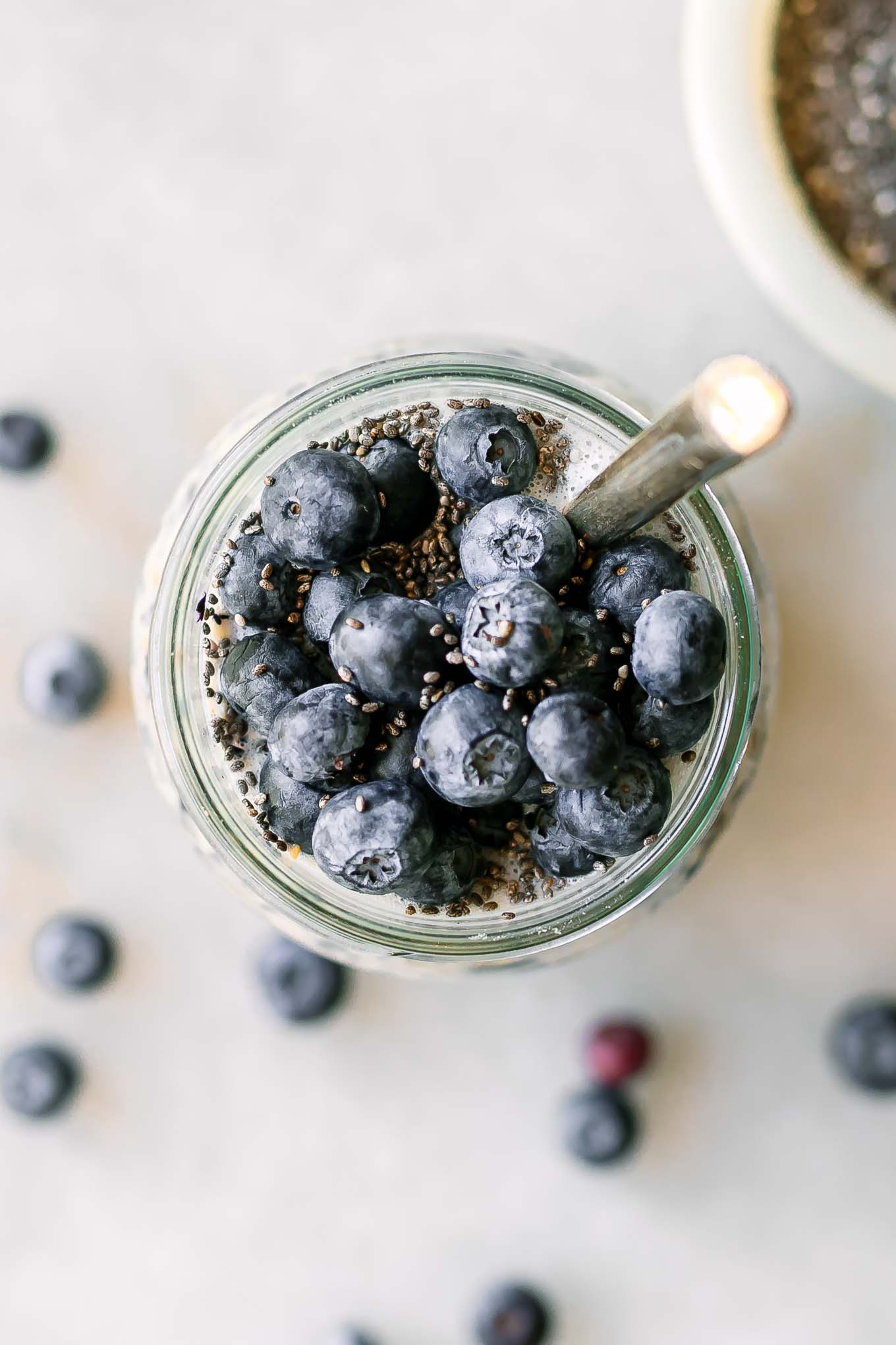 a close up photo of the top of a jar of overnight oats garnished with blueberries and a gold spoon