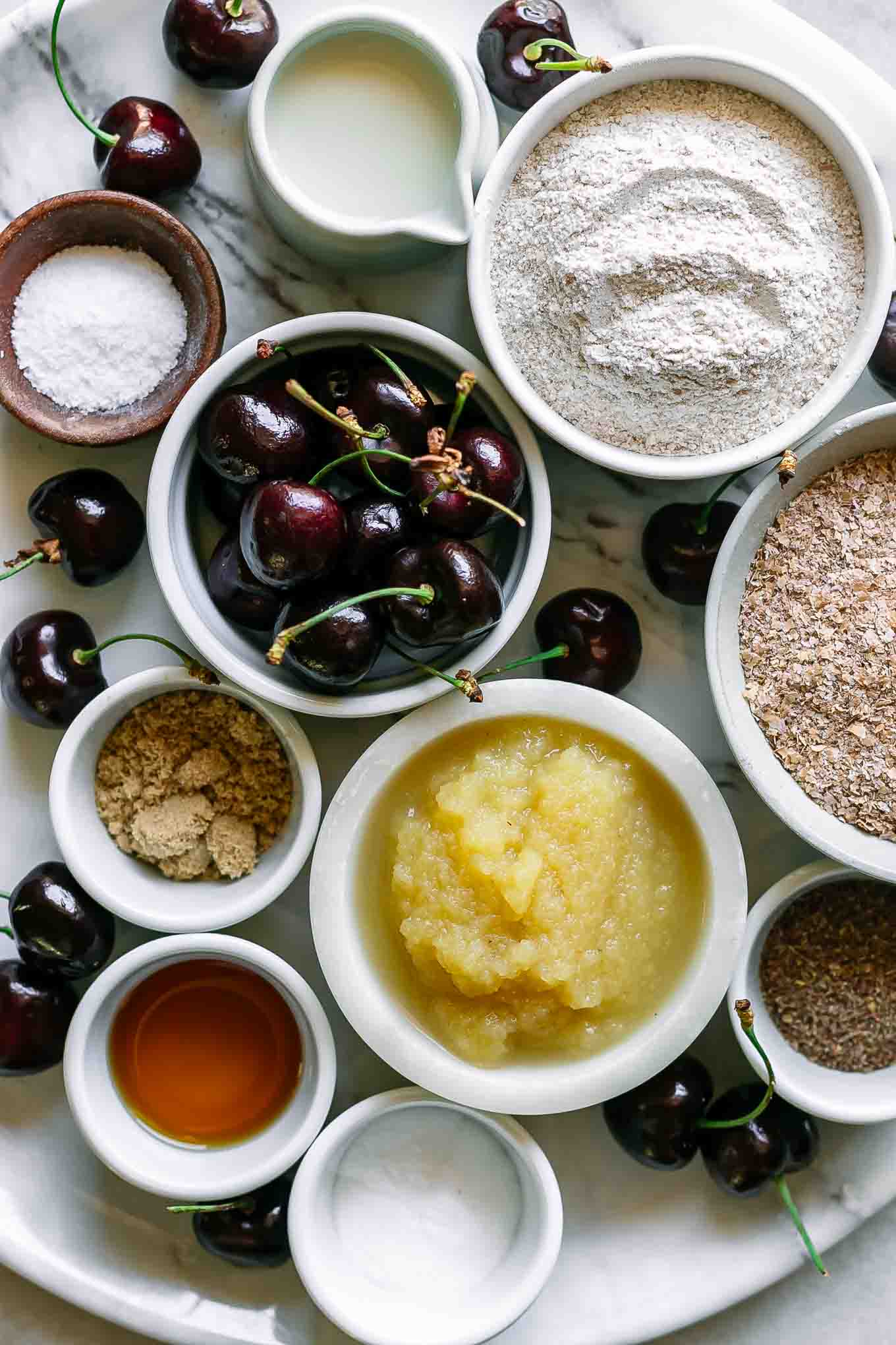 bowls of flour, wheat bran, applesauce, cherries, milk, and other ingredients for bran muffins