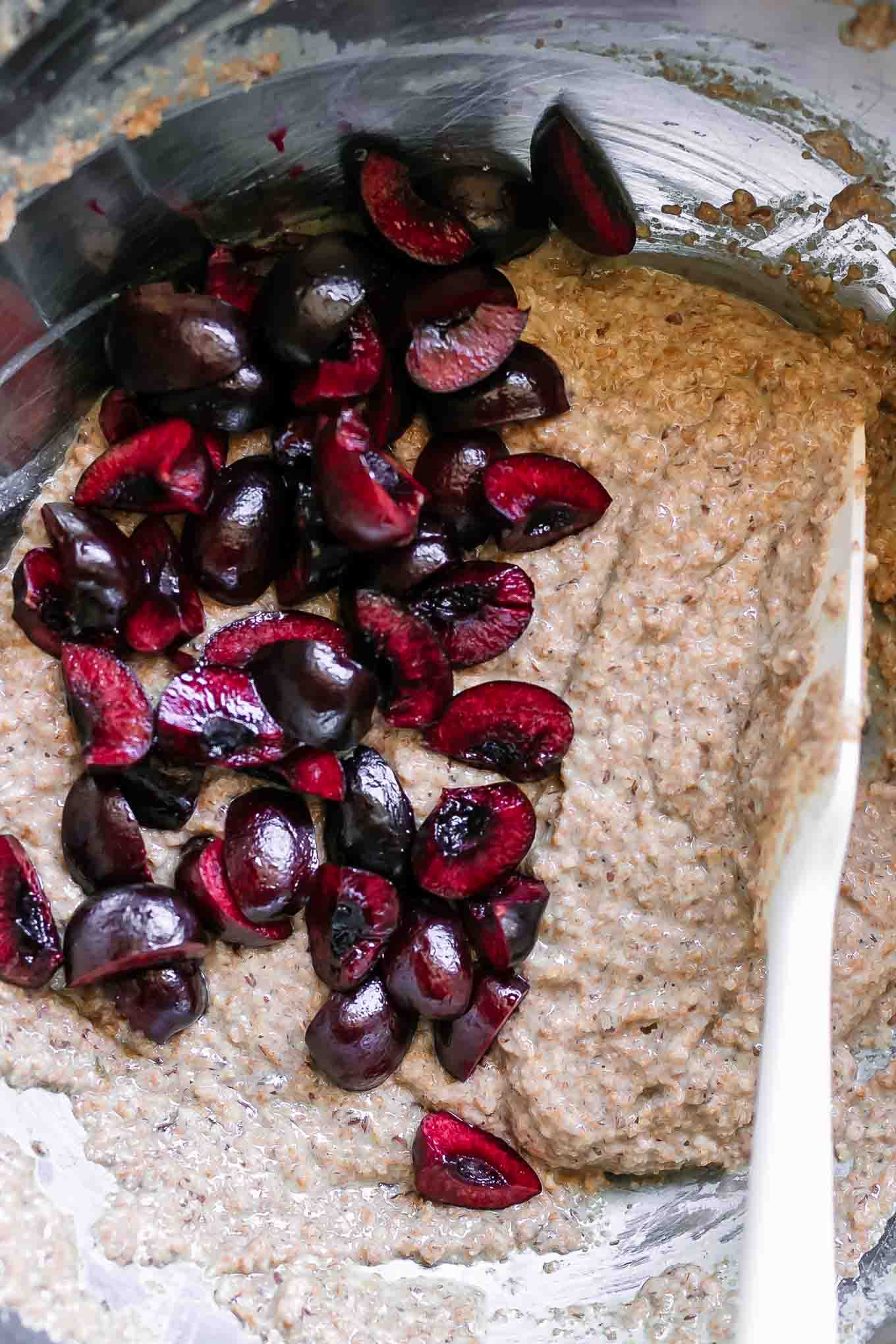 a spatula folding sliced cherries into muffin batter in a mixing bowl