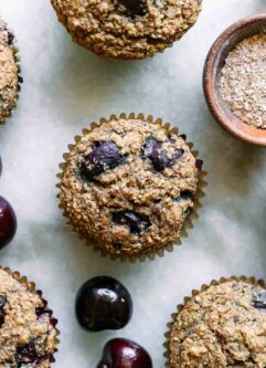 cherry bran muffins on a white table with fresh cherries