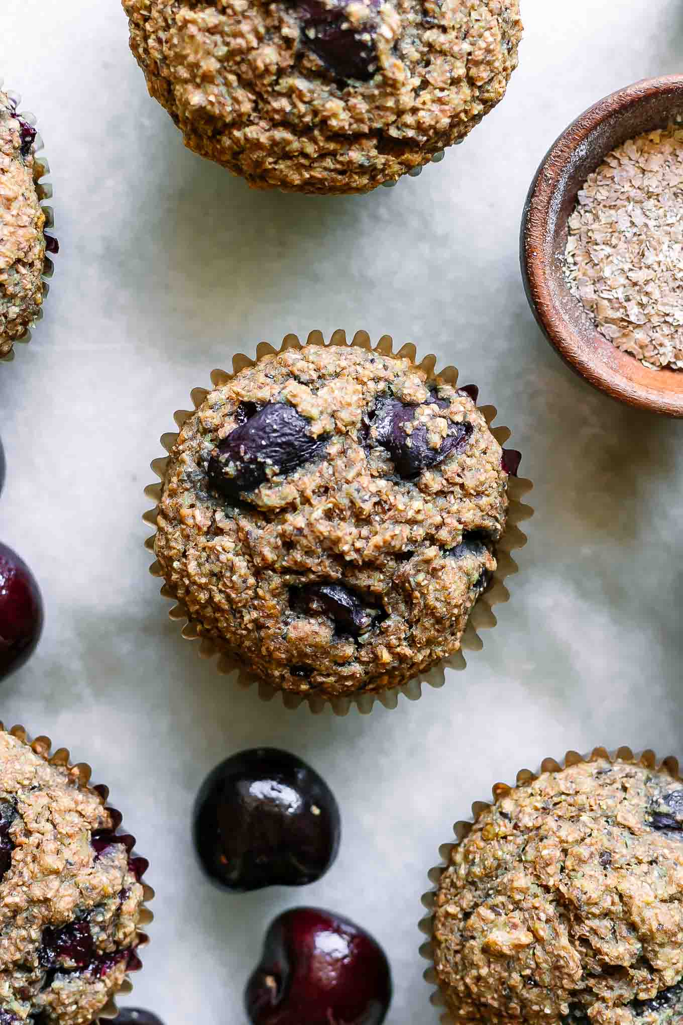 cherry bran muffins on a white table with fresh cherries