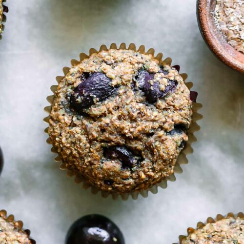 cherry bran muffins on a white table with fresh cherries and a bowl of wheat bran
