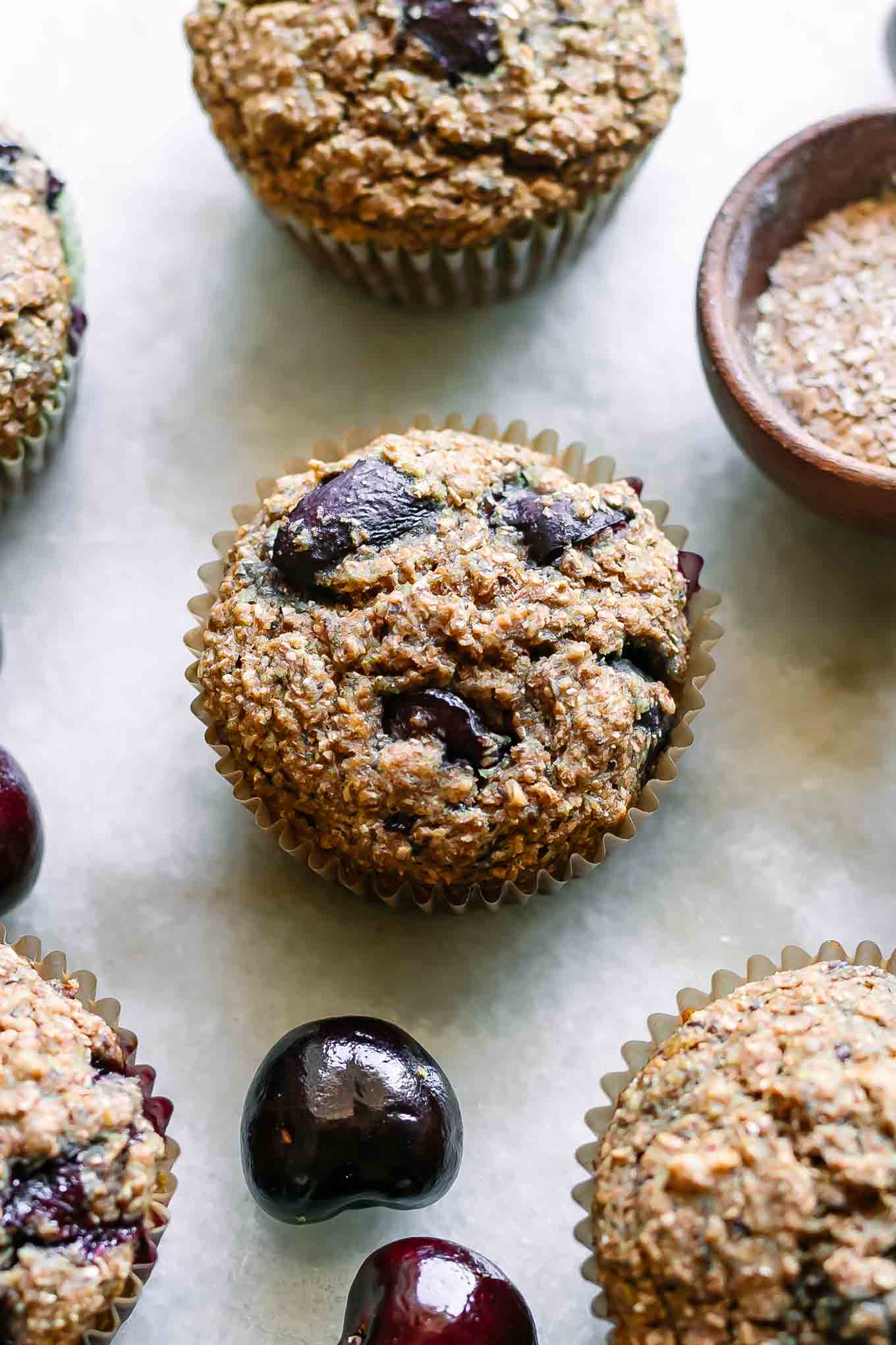 bran muffins with cherries on a white table with fresh cherries