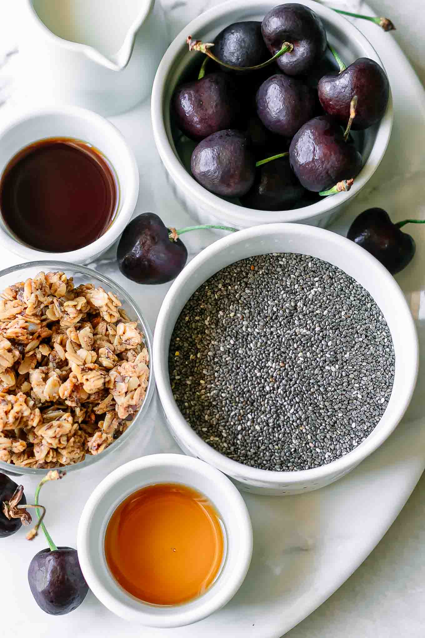 bowls of chia seeds, cherries, granola, milk, and vanilla for chia seed pudding