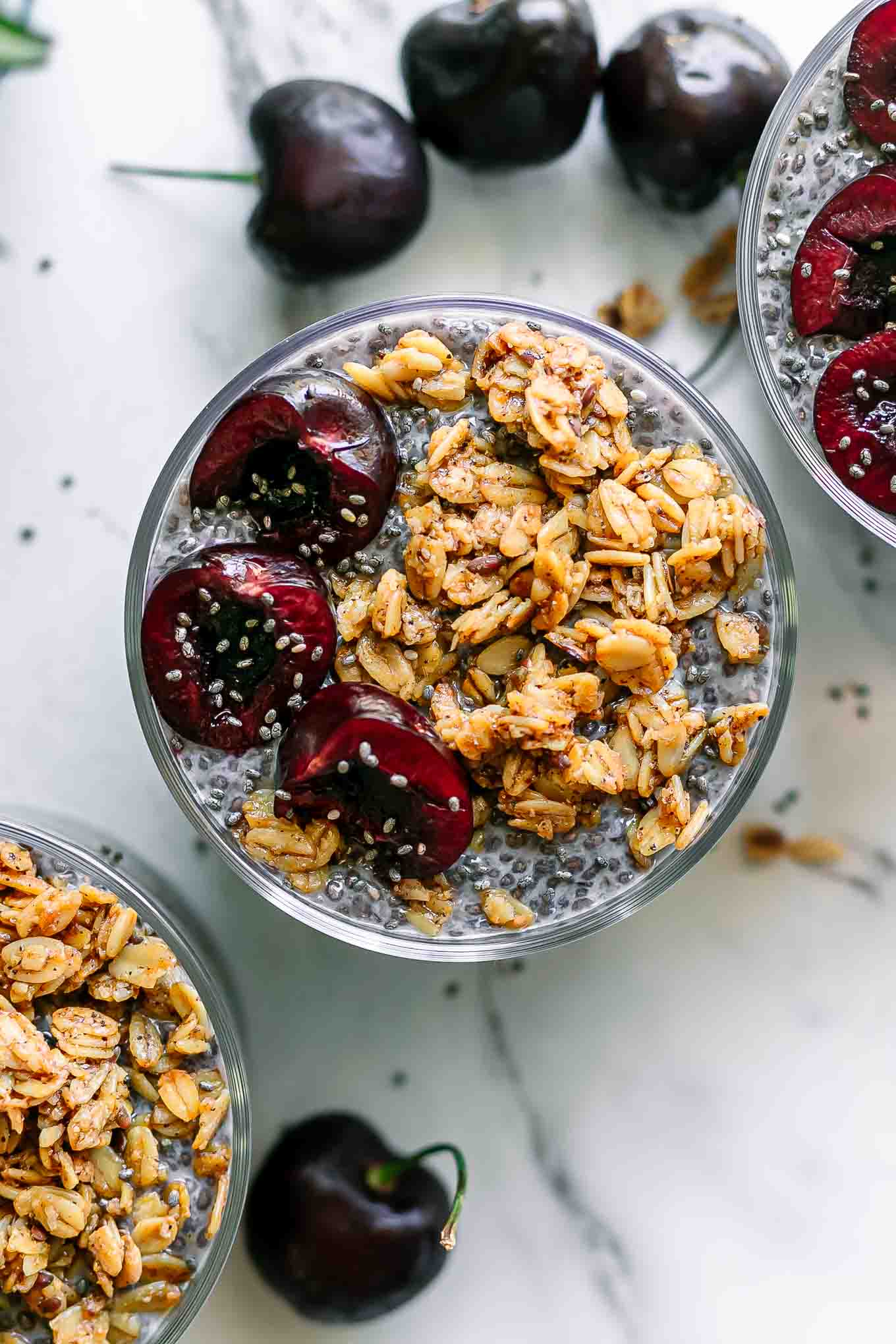 chia seed pudding garnished with granola and cherries on a white table