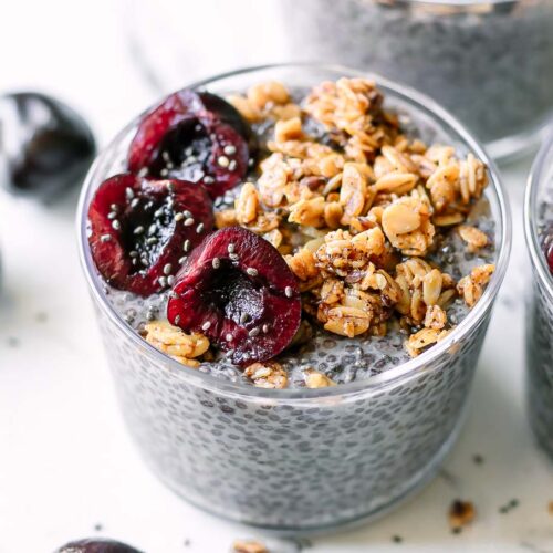 a bowl of cherry chia seed pudding with cherries and granola garnish on a white table