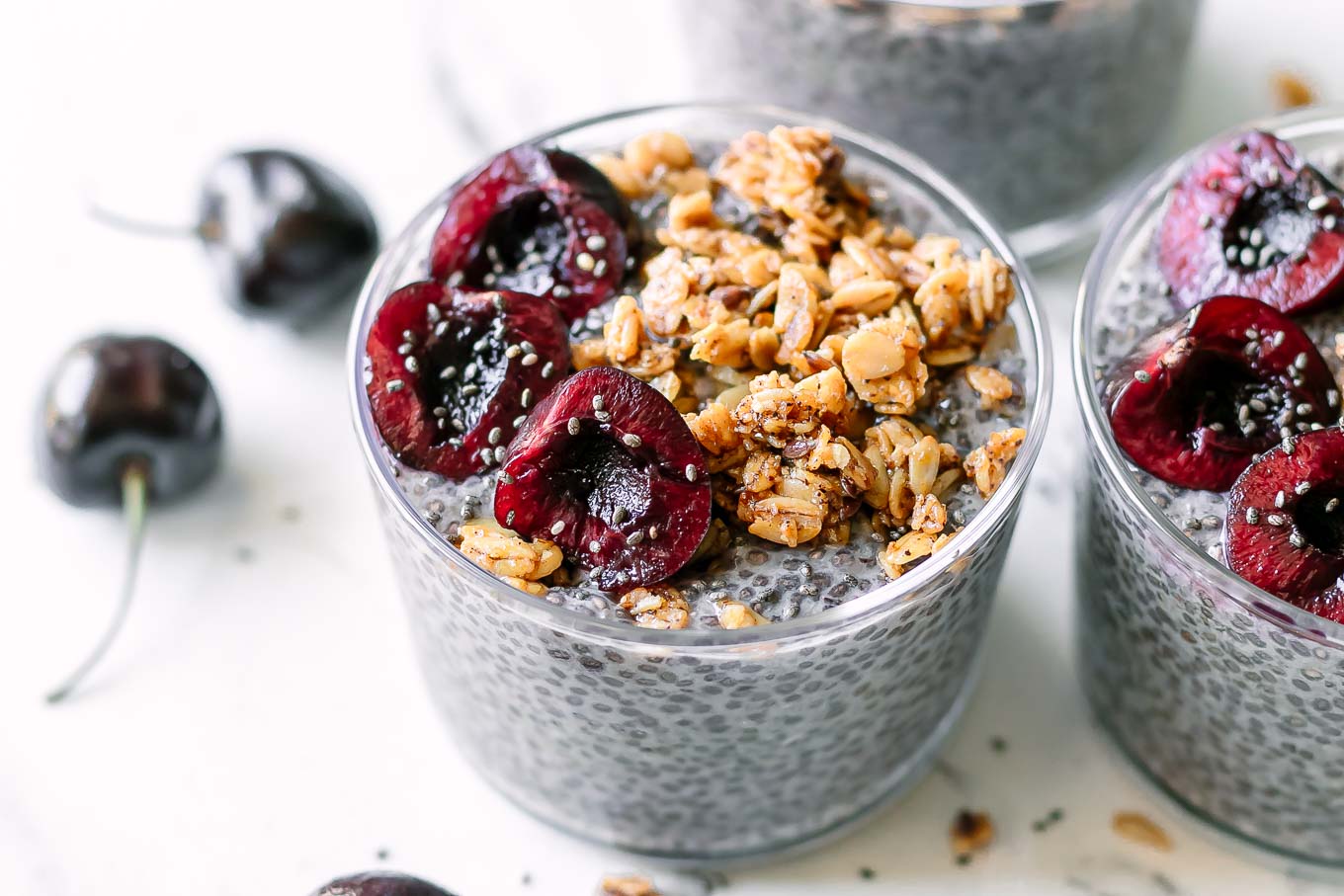 a bowl of cherry chia seed pudding with cherries and granola garnish on a white table