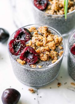 a glass bowl of purple chia pudding made from cherries with granola and sliced cherries on top