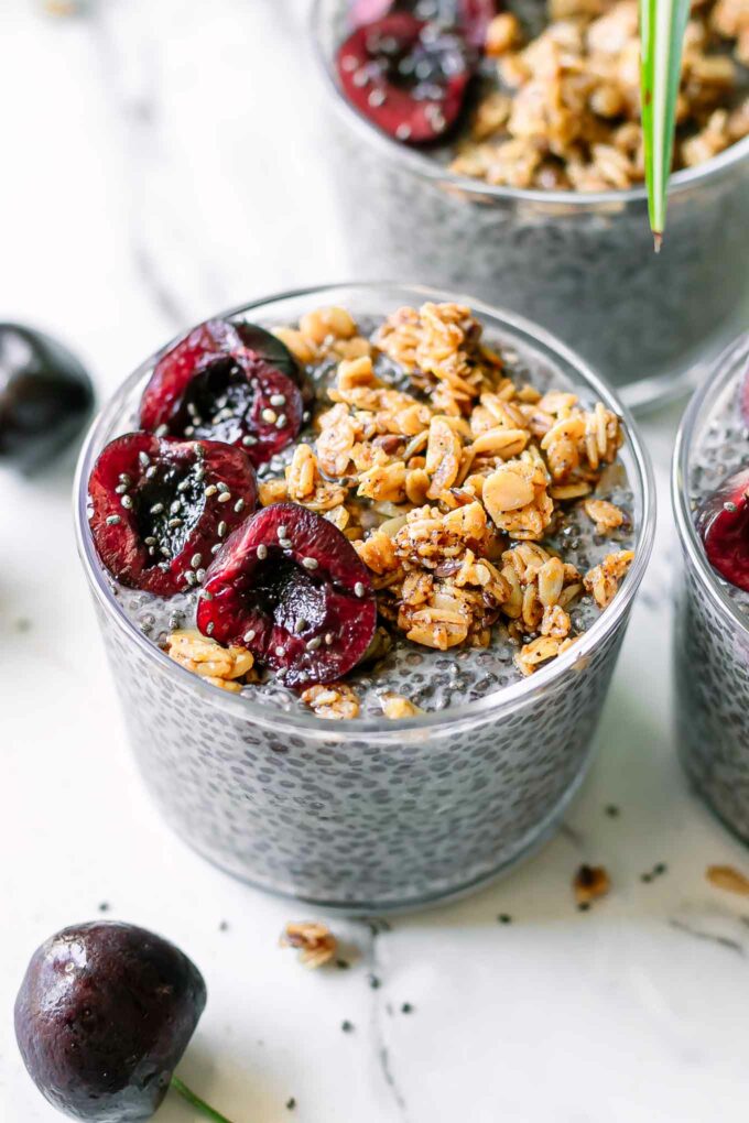 a glass bowl of purple chia pudding made from cherries with granola and sliced cherries on top