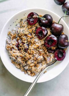 a bowl of cherry oatmeal with sliced cherries on top on a white table