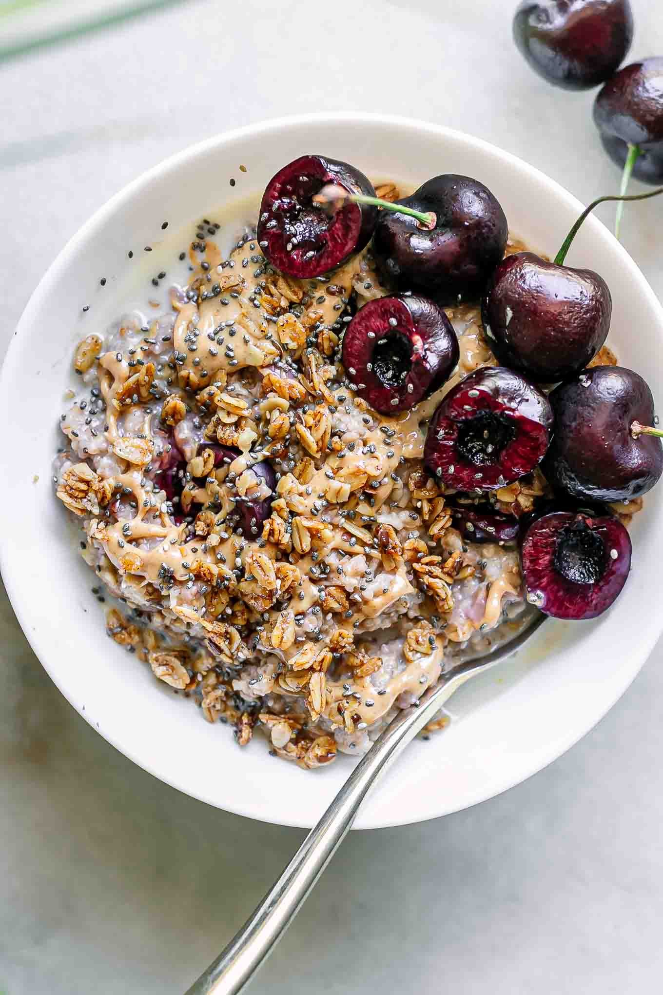 a bowl of cherry oatmeal with sliced cherries on top on a white table