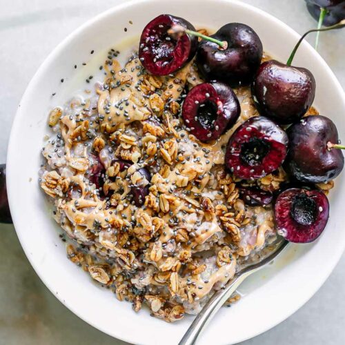 cherry oatmeal with sliced cherries and granola in a white bowl with a gold fork