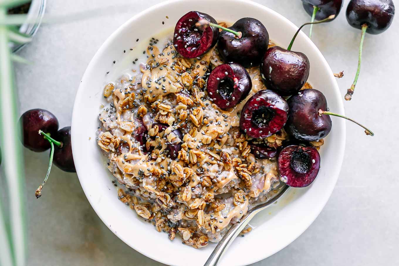 cherry oatmeal with sliced cherries and granola in a white bowl with a gold fork