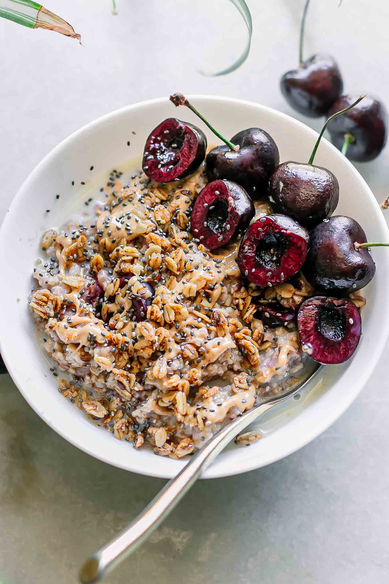 cherry oatmeal bowl with sliced cherries, granola, and drizzled nut butter on a white table