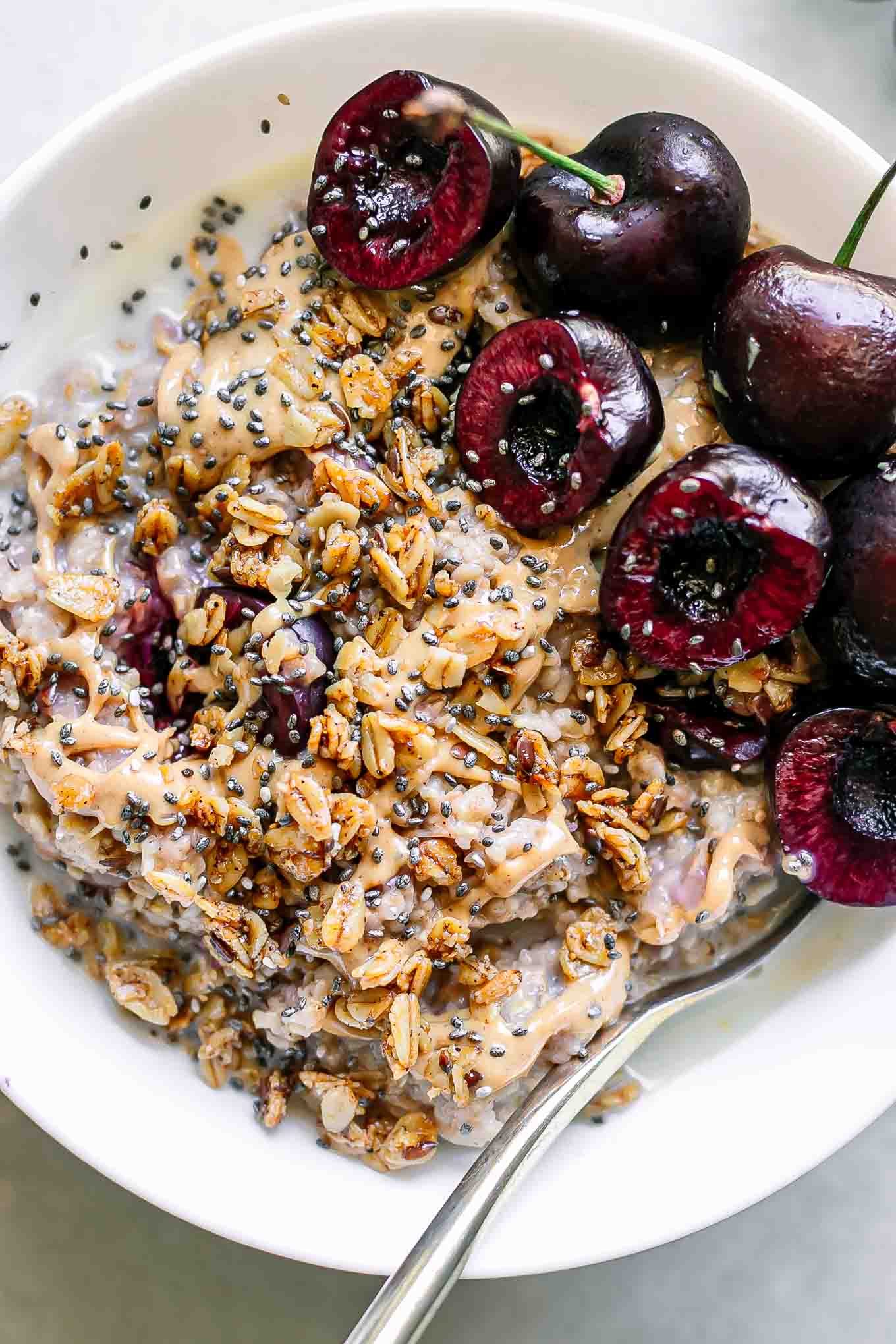 a close up of a bowl of oatmeal with sliced cherries and granola