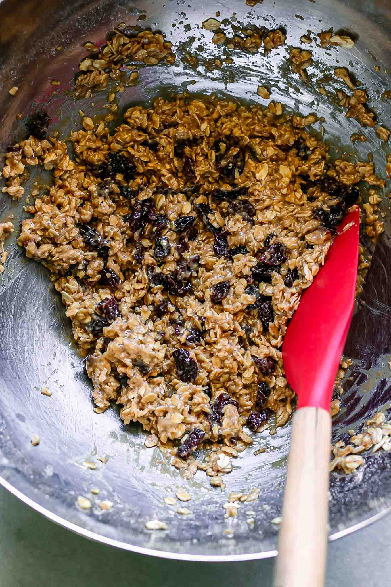 oatmeal cookie batter with dried cherries in a mixing bowl with a baking spatula