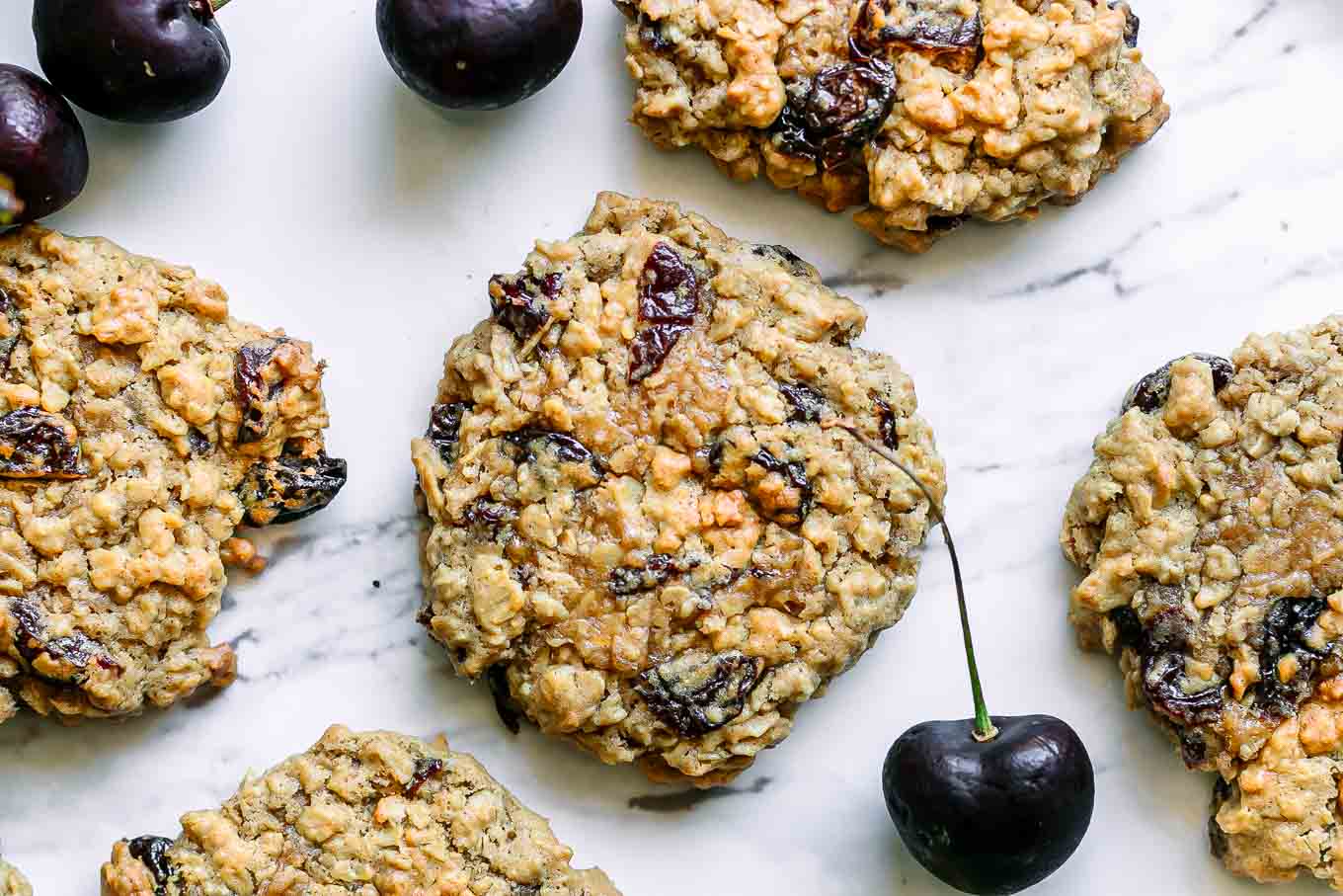 vegan cherry oatmeal cookies on a white table with fresh cherries