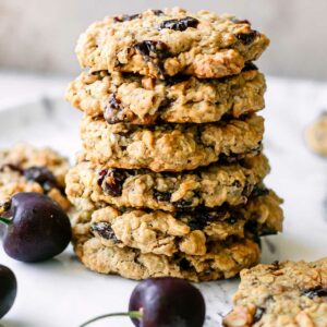 stacked plant-based cherry oatmeal cookies on a white table with fresh black cherries