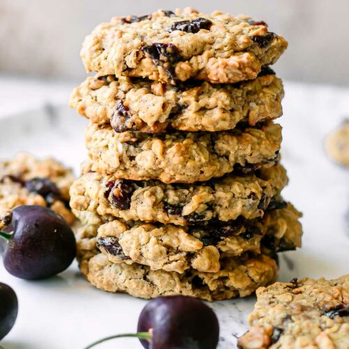 stacked plant-based cherry oatmeal cookies on a white table with fresh black cherries