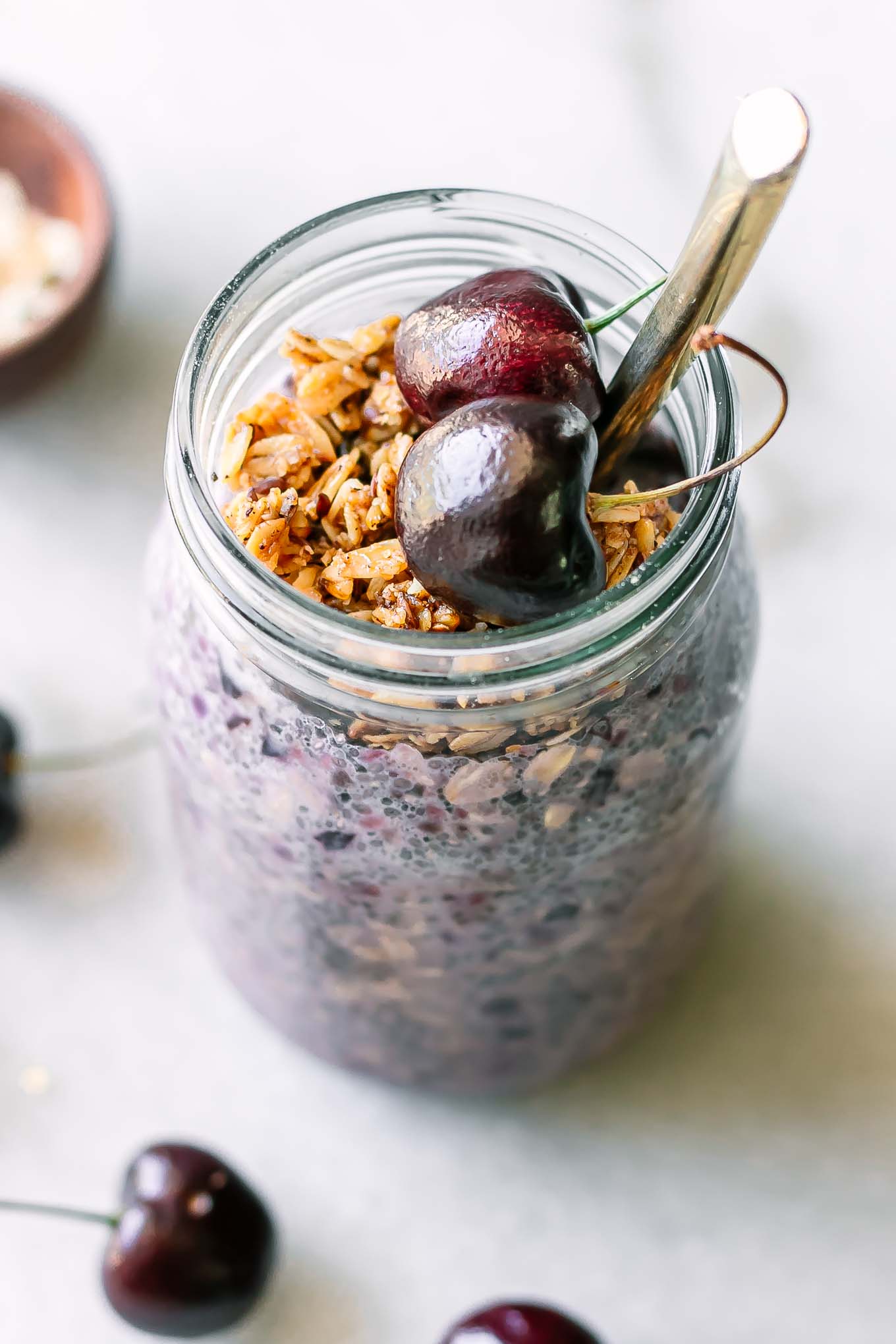 a jar of purple colored overnight oats garnished with fresh cherries on a white table