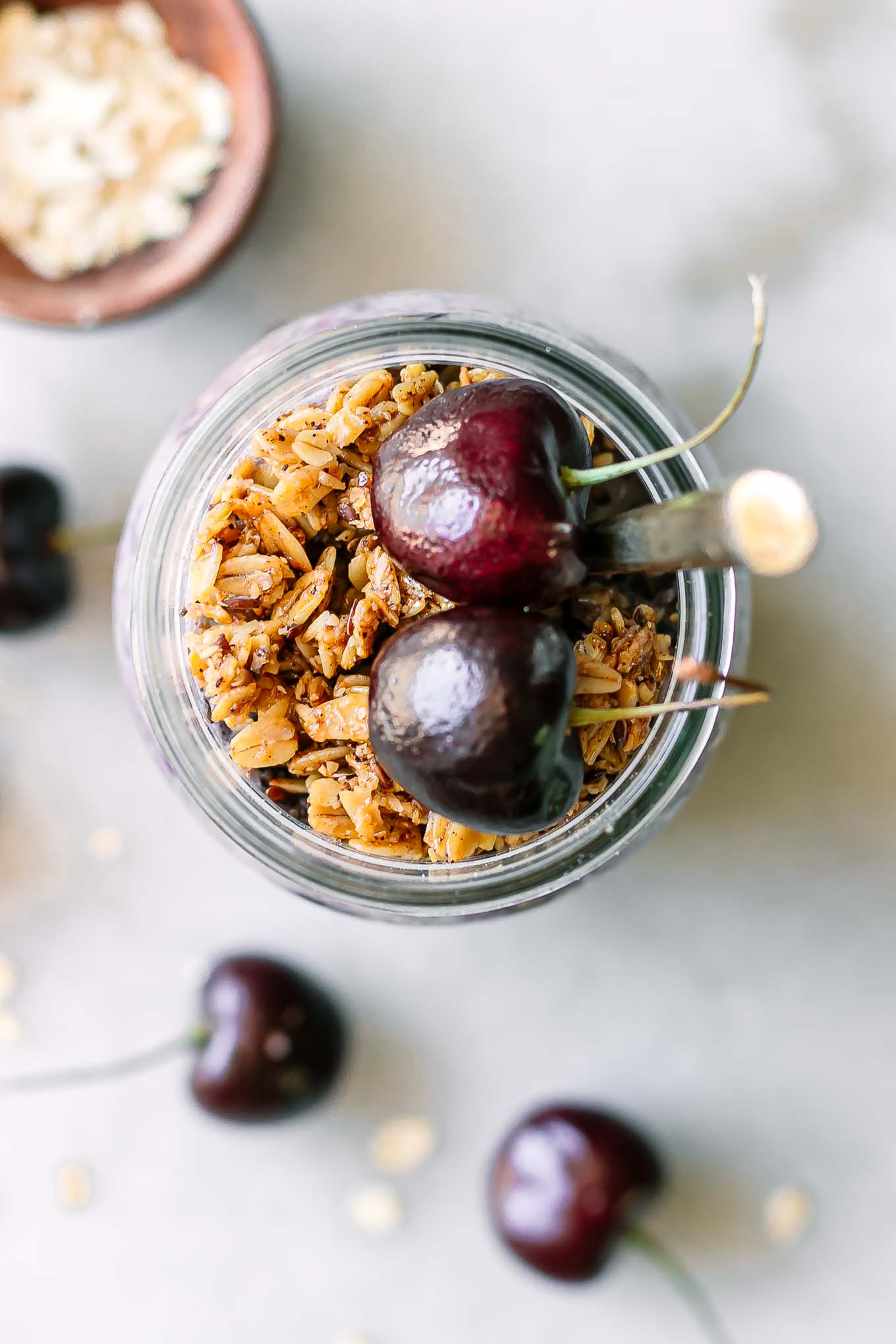 overnight oats in a jar garnished with granola and fresh cherries on a white table