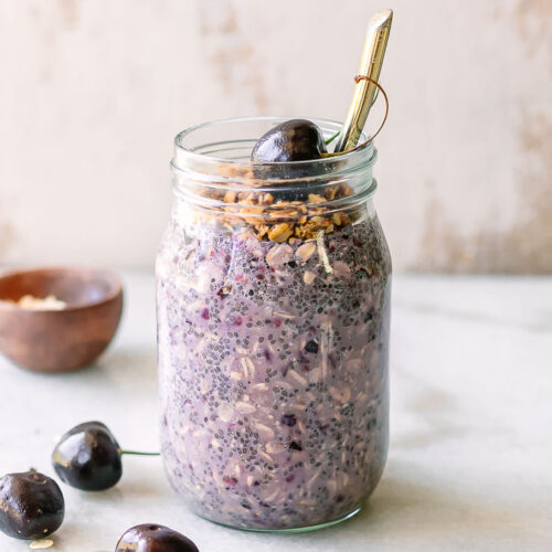 a mason jar of cherry overnight oats with cherries and granola garnish on a white table