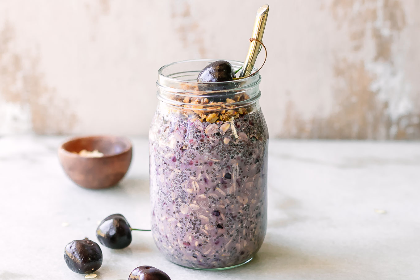 a mason jar of cherry overnight oats with cherries and granola garnish on a white table