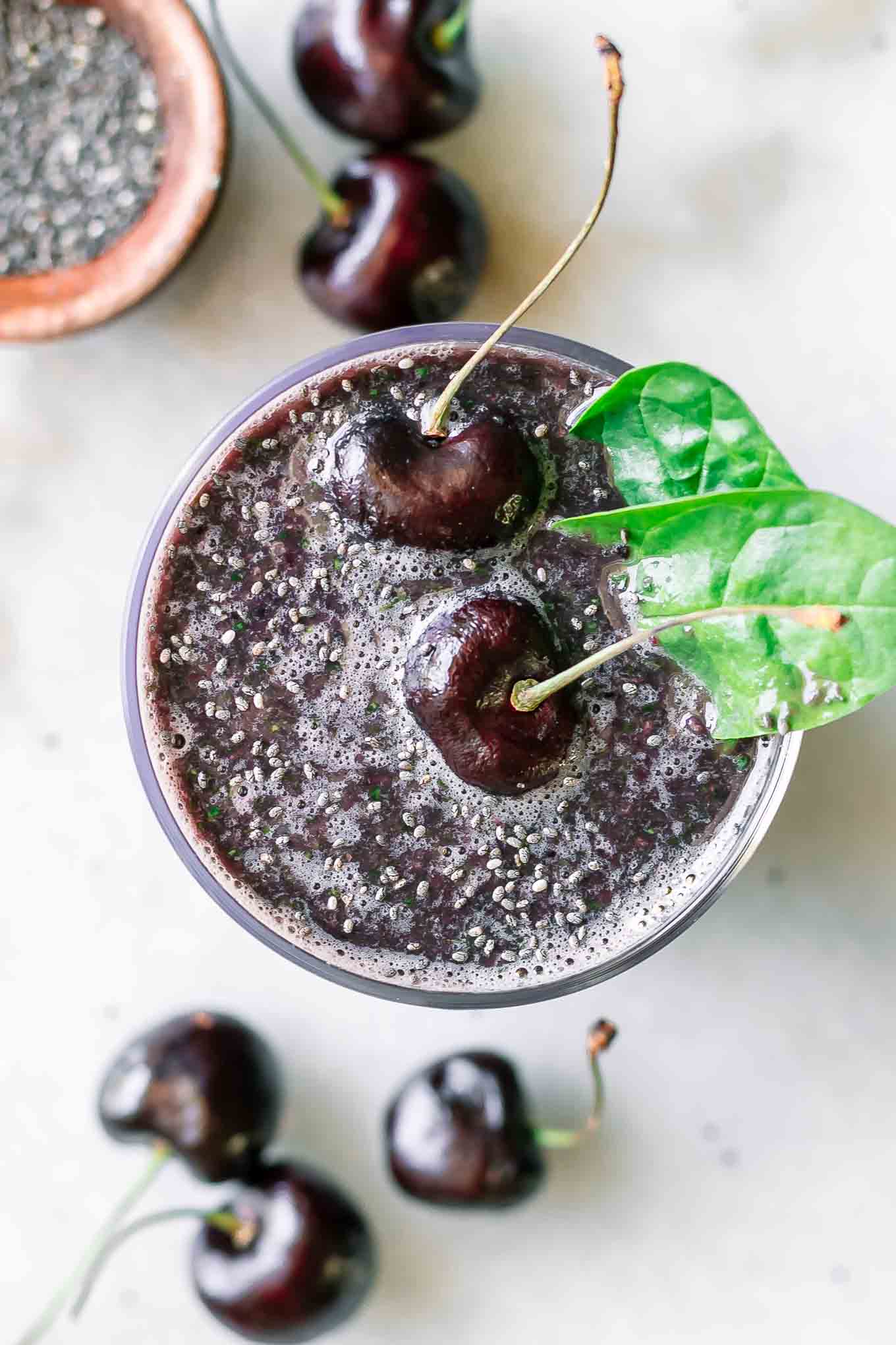 a cherry spinach smoothie with cherries and spinach garnish on a white table