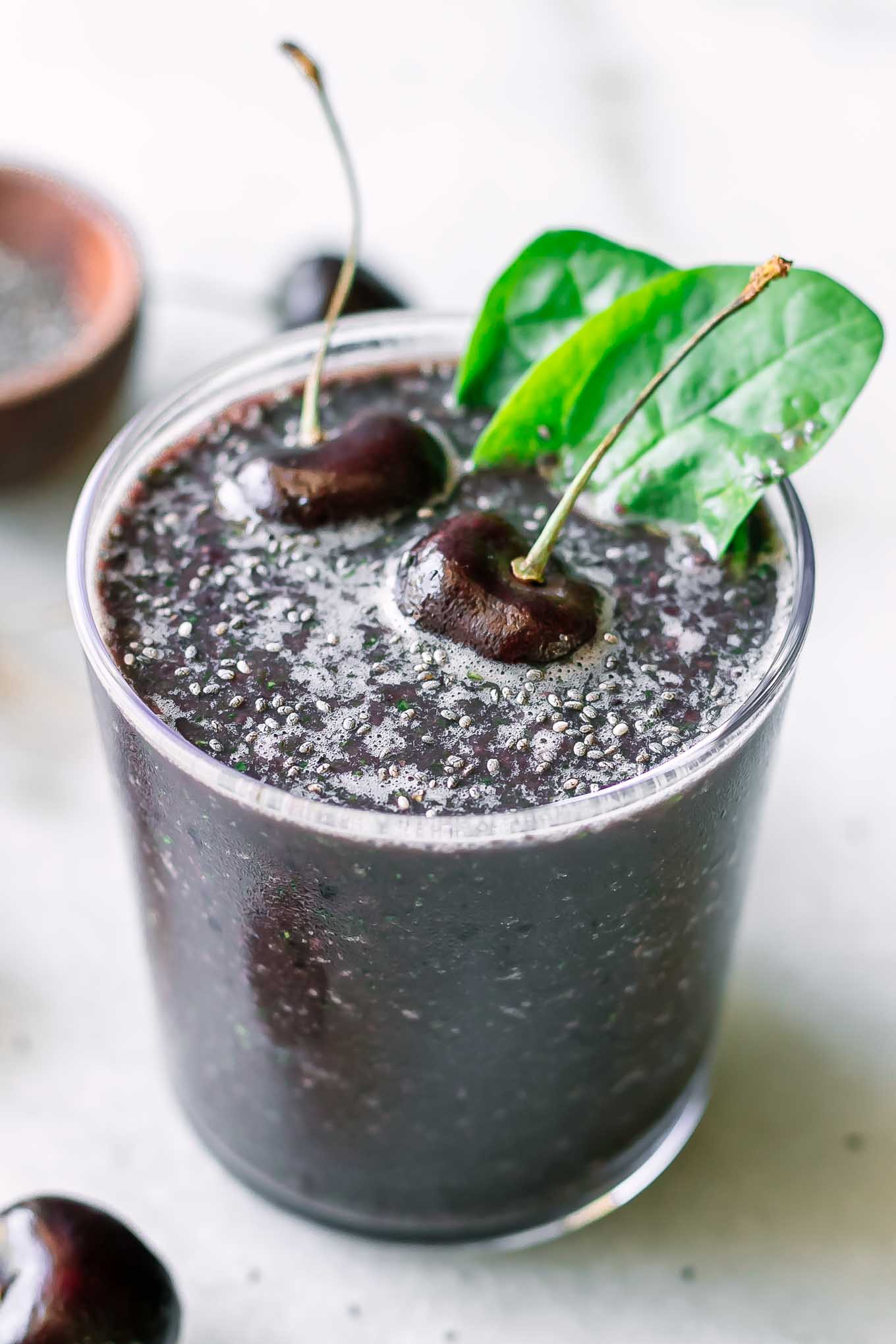 a purple smoothie with cherries and spinach on a white table with fresh cherries