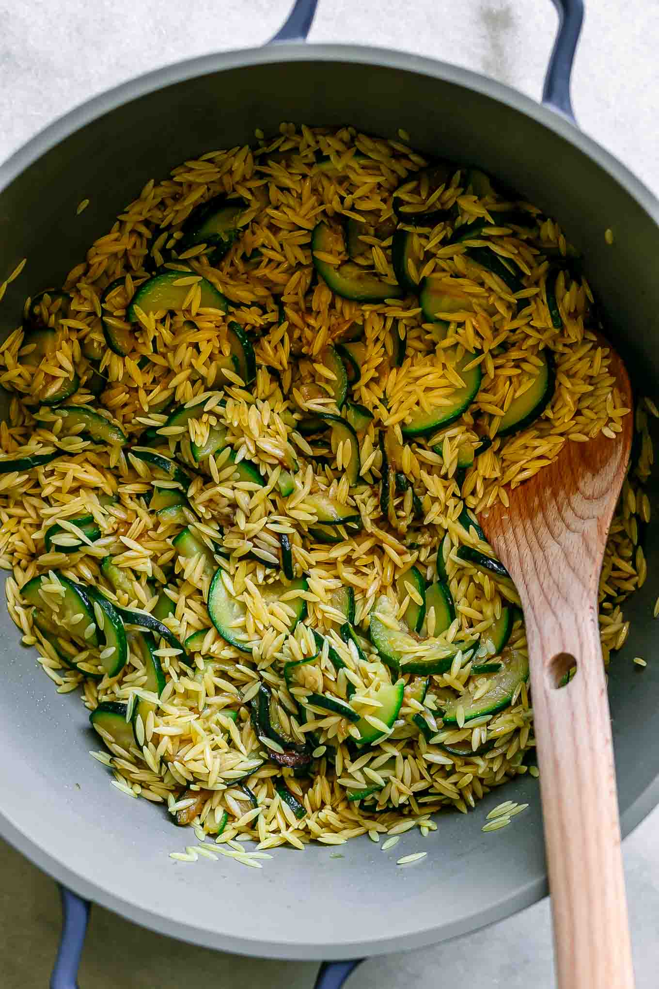 dry orzo with zucchini stirring in a large pot with a wooden spoon